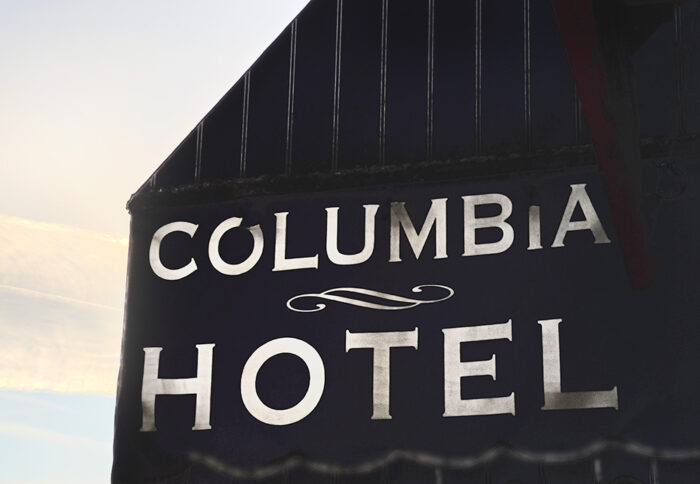 Black facade of Columbia Hotel with bold white lettering against a glowing sky – Fred Gerendasy Photography