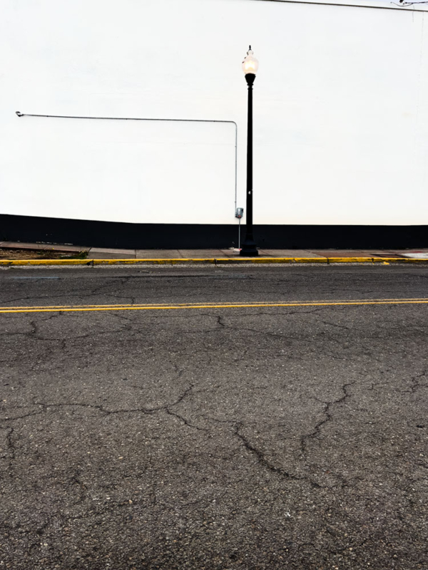 Across the street, a view of a stark black lamppole against a white wall
