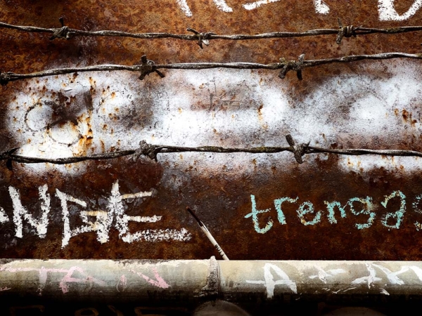 Deep brown rusted metal, graffiti and barbed wire in front