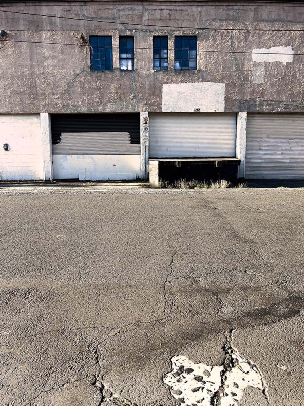 Empty lot with cracked concrete and strong filtered light across side of old concrete walled building