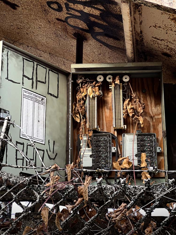 old circuit breakers under a bridge with barbed wire fence in front of it