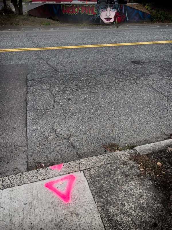 low shot of road, cartoon woman on curb next to painted lucky devil sign