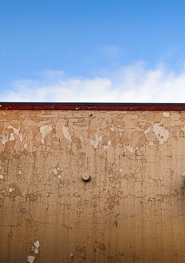 Wall of peeling brown paint amidst a patch of blue sky with puffy diffuse clouds