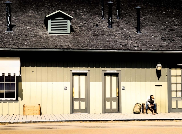 An old railroad building with a weary traveler sitting outside on the porch.